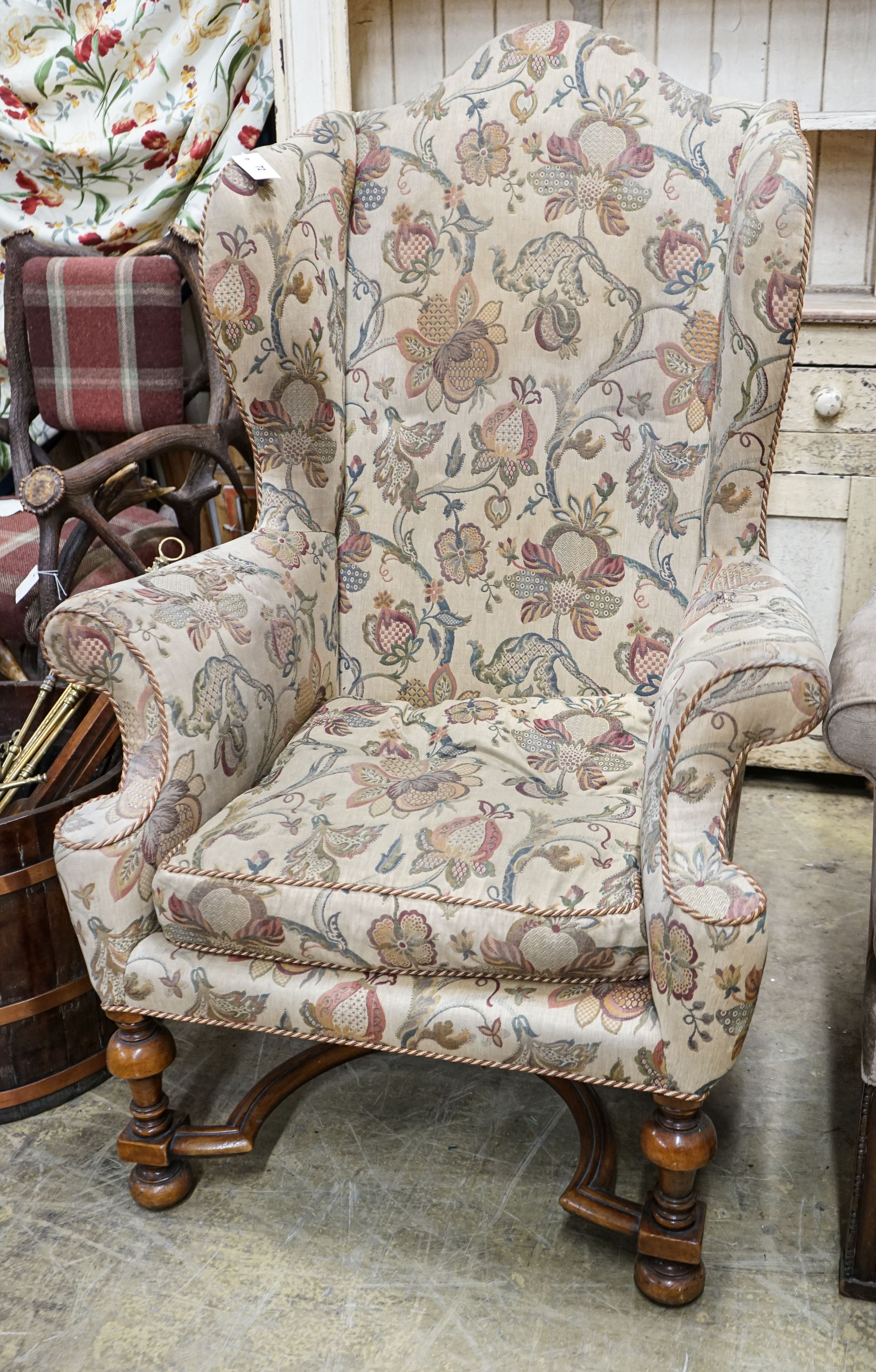 A William & Mary style walnut wing armchair, with flowering scroll upholstery and turned underframe with serpentine stretcher, width 86cm, depth 66cm, height 130cm